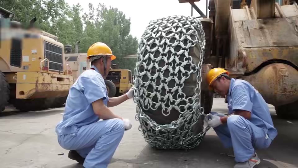 Two workers positioning a protection chain around a loader tire