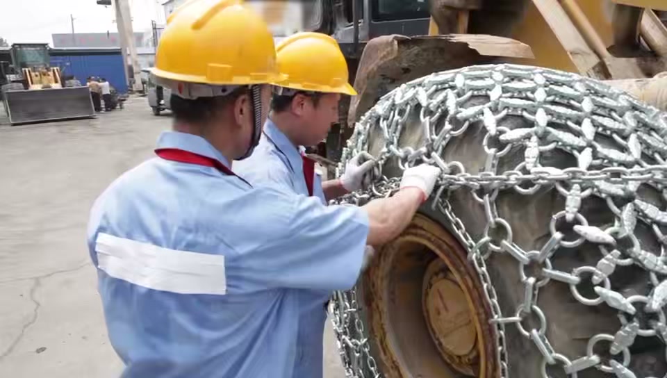 Workers adjusting the side chain along a loader tire